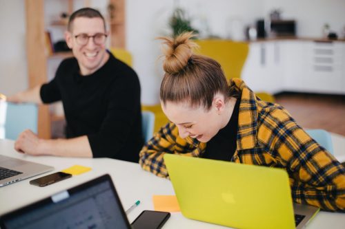 man-and-woman-laughing-whilst-working-on-laptops