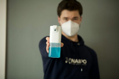 man-in-face-mask-holding-up-a-bottle-of-hand-sanitiser