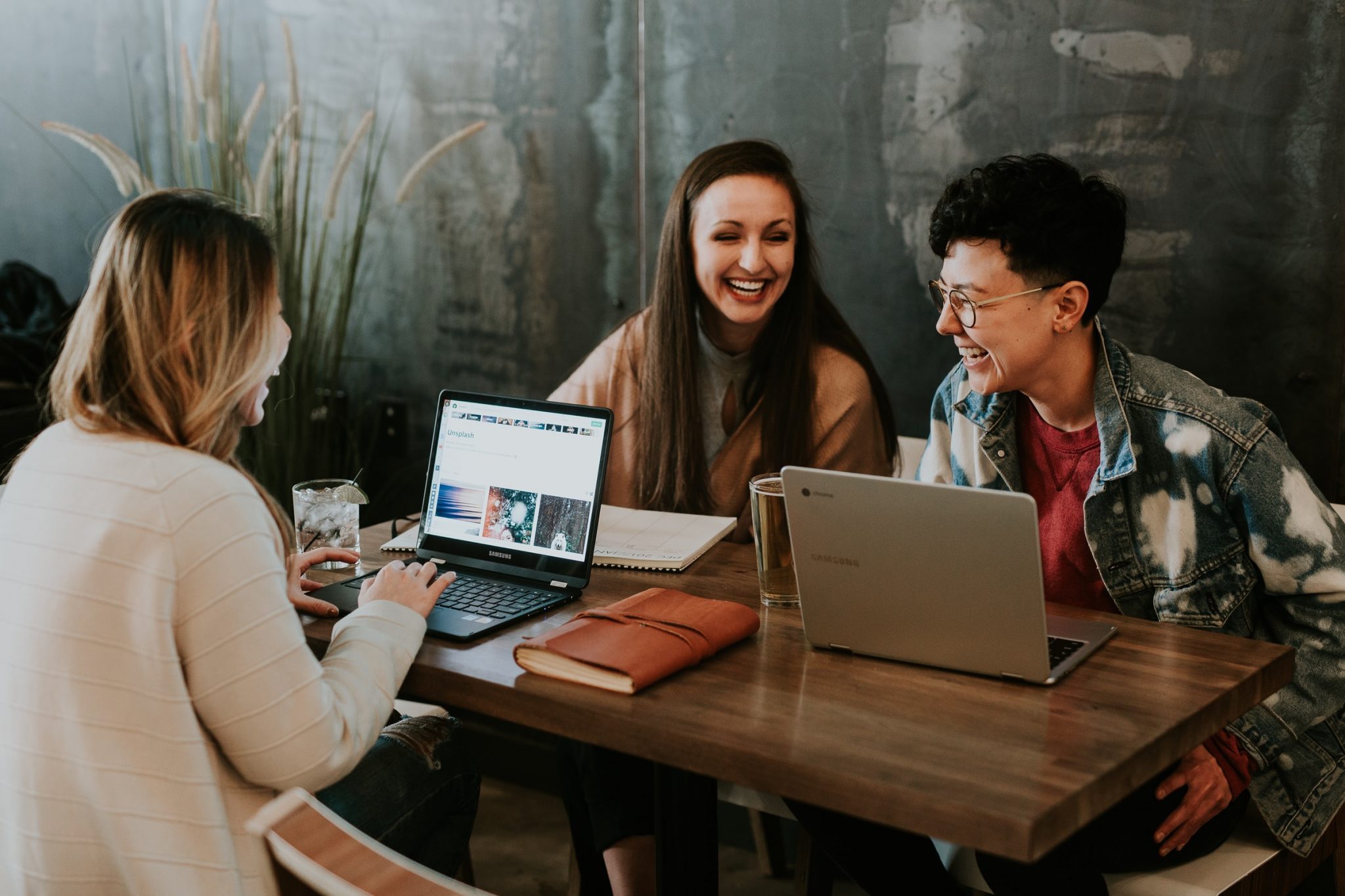 three-employees-sitting-at-a-table-on-their-laptops-enjoying-their-work