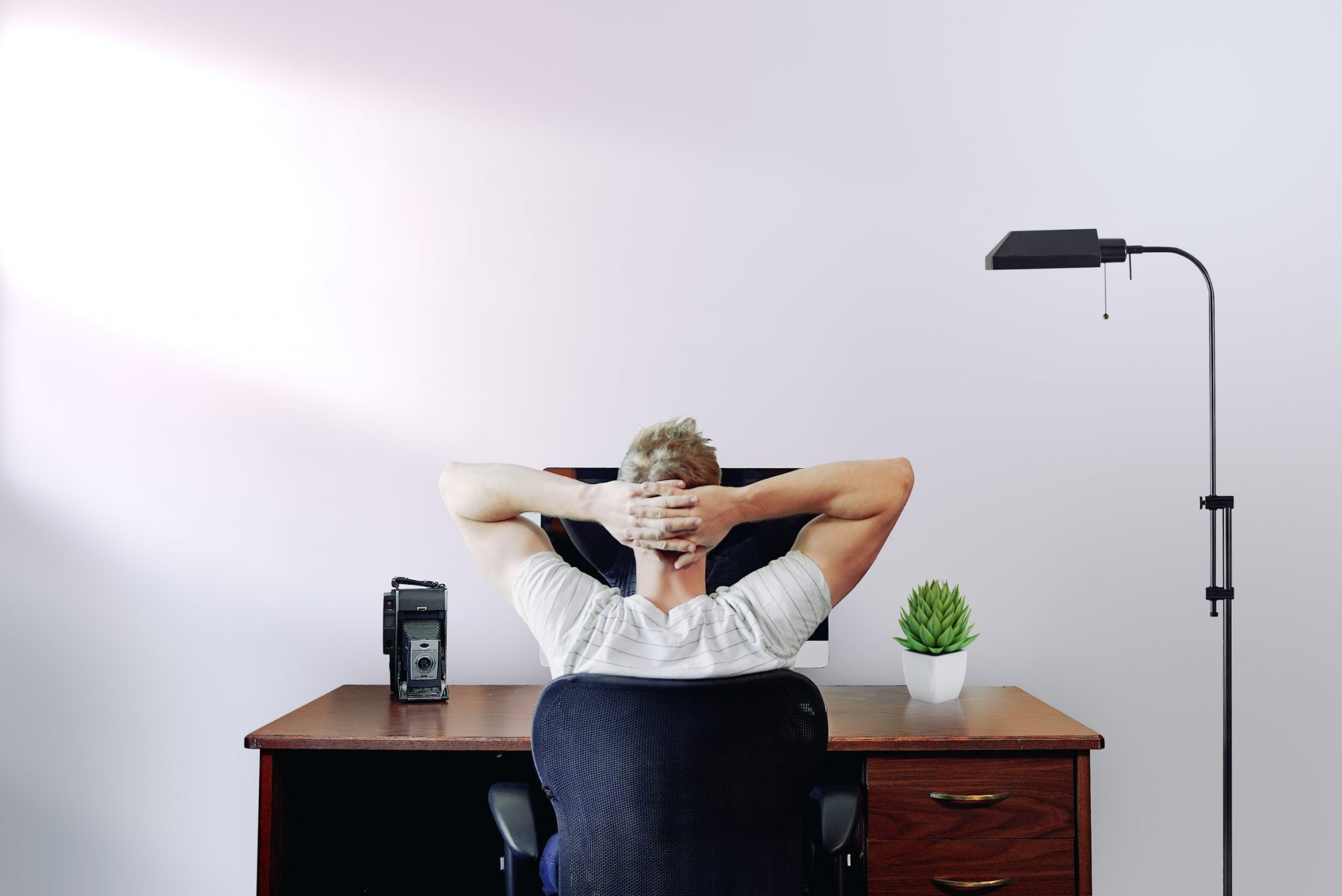 man-sat-at-a-desk-with-arms-behind-his-head