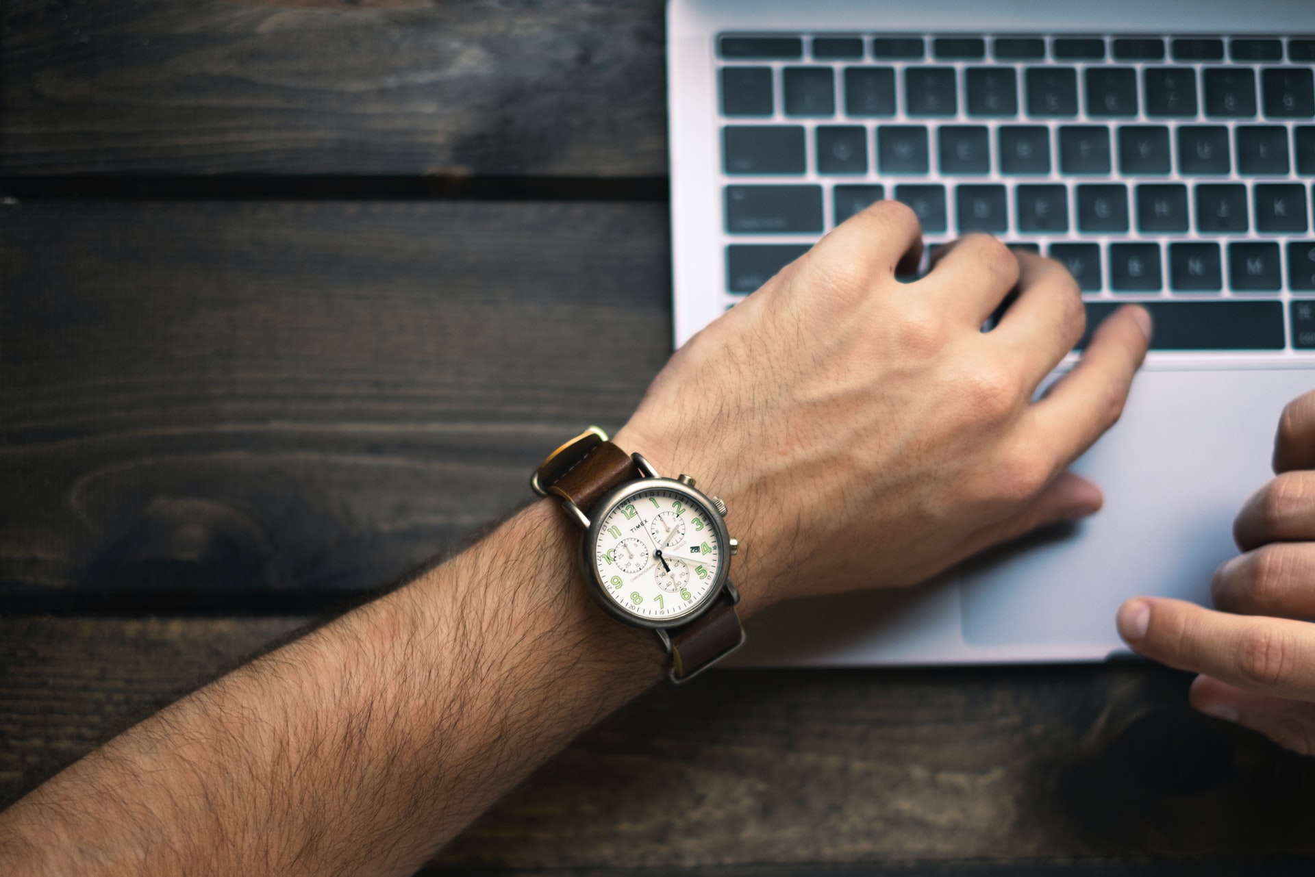 an-image-of-a-person-looking-at-a-watch-whilst-working-on-a-laptop