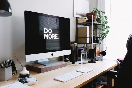 an-image-of-a-tidy-work-desk-with-an-imac-displaying-the-text-do-more-on-the-screen