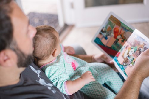 man-sitting-down-with-baby-on-his-chest-reading-a-childrens-book