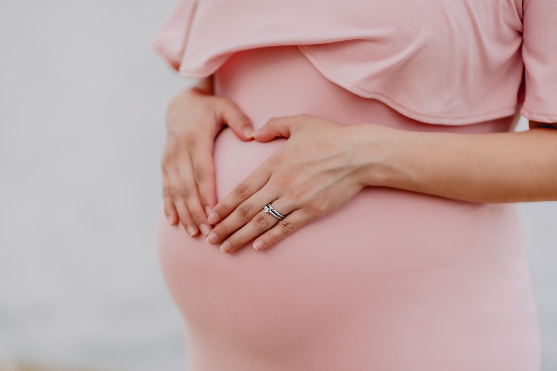 pregnant-woman-wearing-a-pink-dress-holding-her-belly-wearing-a-wedding-ring