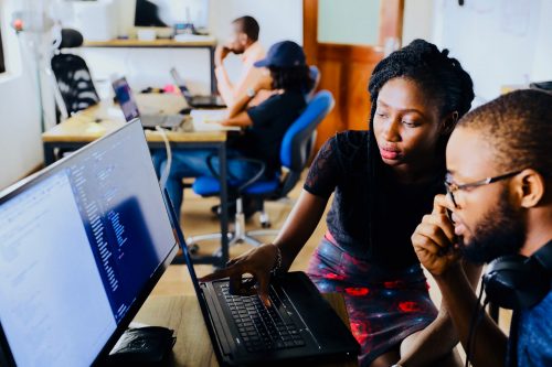 two-people-working-at-a-computer-with-others-working-in-the-background