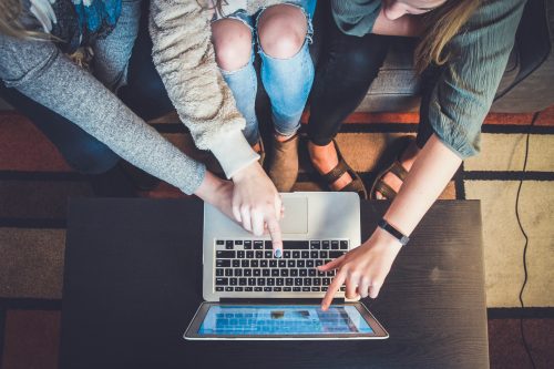 three-people-pointing-at-a-computer-screen-pictured-from-above