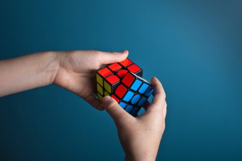 persons-hands-solving-a-rubix-cube-against-a-blue-background