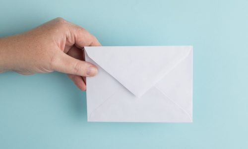 a-hand-holding-an-envelope-in-front-of-a-pale-blue-background