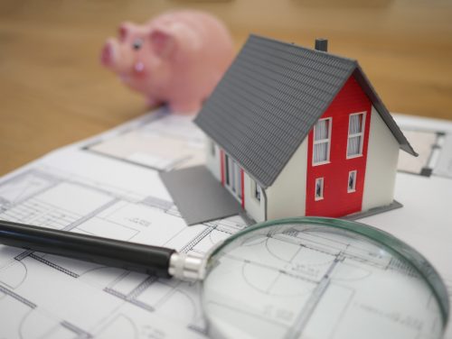 image-of-a-small-house-model-a-magnifying-glass-and-a-piggy-bank-sitting-on-top-of-a-blueprint
