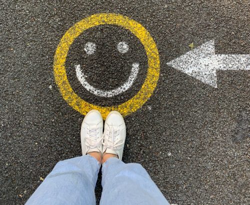 shot-of-a-smiley-face-on-a-road-with-an-arrow-pointing-at-it-and-someone-standing-underneath