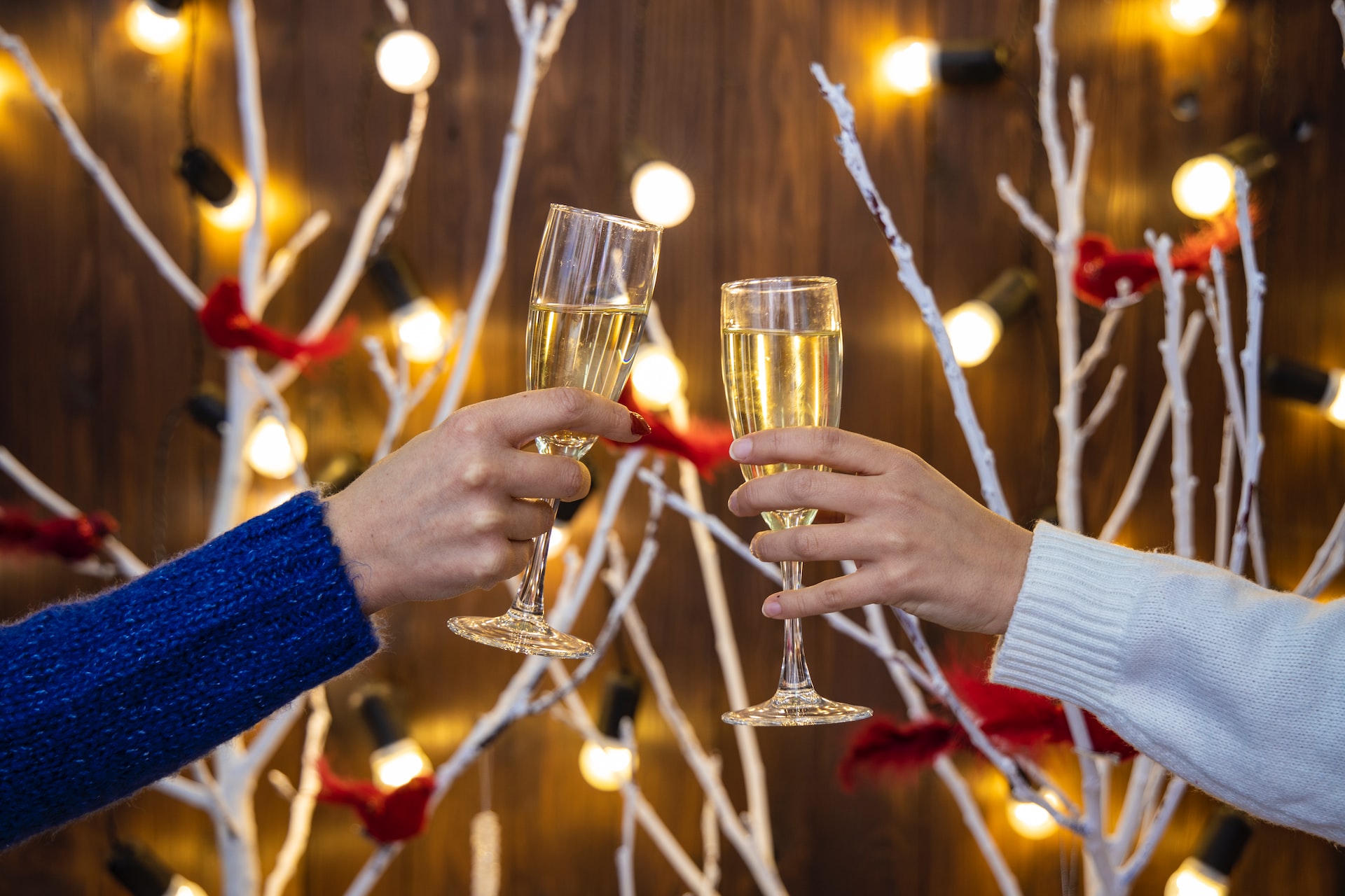 two-people-holding-glasses-of-champagne-up-for-a-toast-with-christmas-decorations-in-the-background