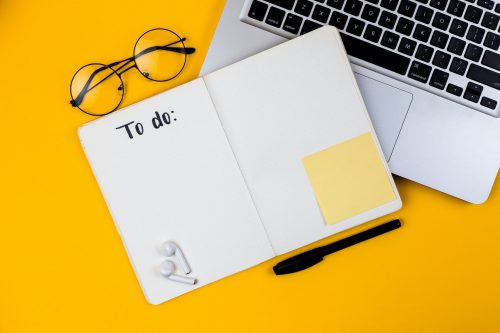 bright-yellow-background-image-with-a-laptop-pair-of-glasses-and-a-notebook-and-pen-showing-a-to-do-list