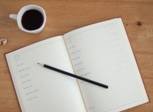 shot-of-a-note-book-with-a-pencil-over-it-and-a-coffee-in-a-mug-above-it