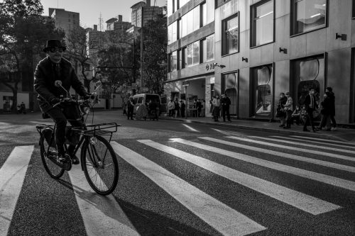 black-and-white-shot-of-a-man-cycling-through-a-town-centre