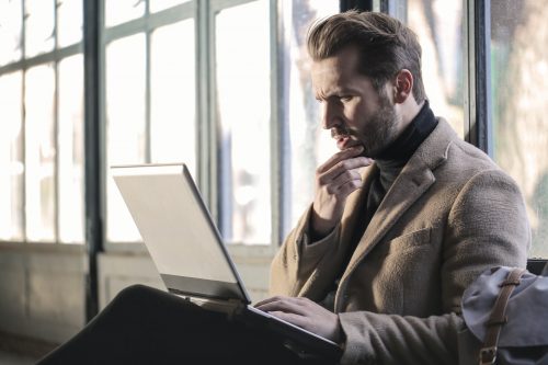 man-sitting-down-looking-at-a-laptop-while-in-a-thinking-pose