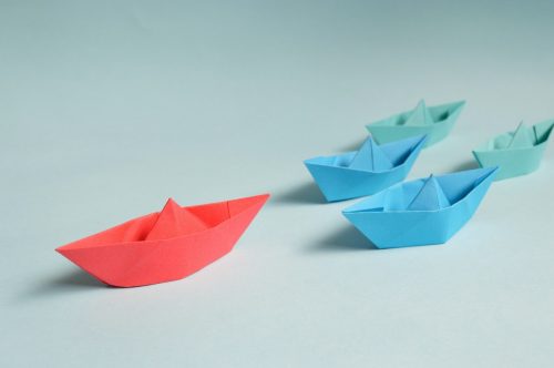 shot-of-small-blue-paper-boats-being-led-forward-by-a-red-paper-boat