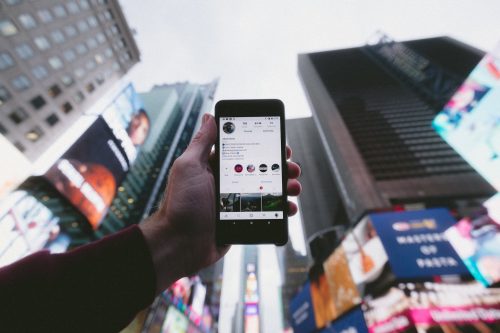 a-hand-holding-out-a-smart-phone-with-a-backdrop-of-high-rise-buildings