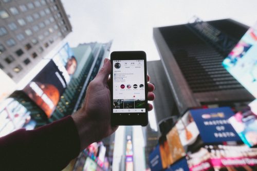 a-hand-holding-out-a-smart-phone-with-a-backdrop-of-high-rise-buildings