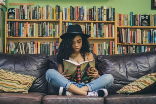 woman-sitting-on-a-leather-sofa-reading-a-book-with-a-bookcase-in-the-background