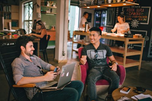image-of-two-people-sitting-in-chairs-in-a-co-working-environment-smiling-and-laughing